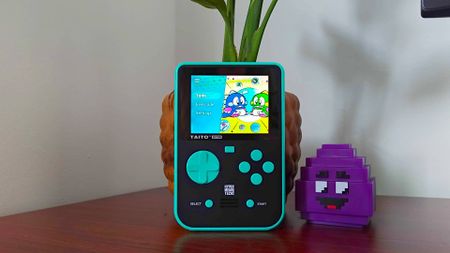 Super Pocket Taito Edition on woodgrain desk leaning against plant next to Grimace Minecraft McDonalds toy.